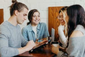 Nonverbal Cues: A group of friends at a coffee shop are talking. EVeryone is engaged in the conversation, except for one who looking at his device.